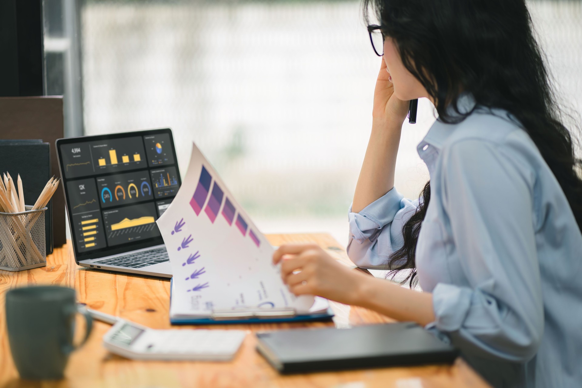 Businesswoman accountant using a calculator, graphs, and charts to analyze market data, balance sheets,accounts,and net profits in order to plan new sales strategies.